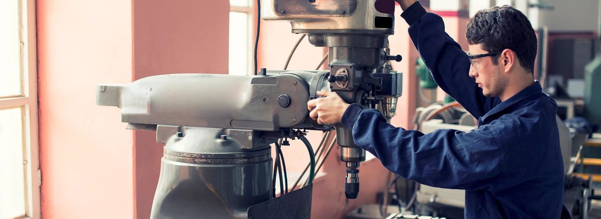 A person in safety glasses and overalls operates a large industrial machine in a workshop.